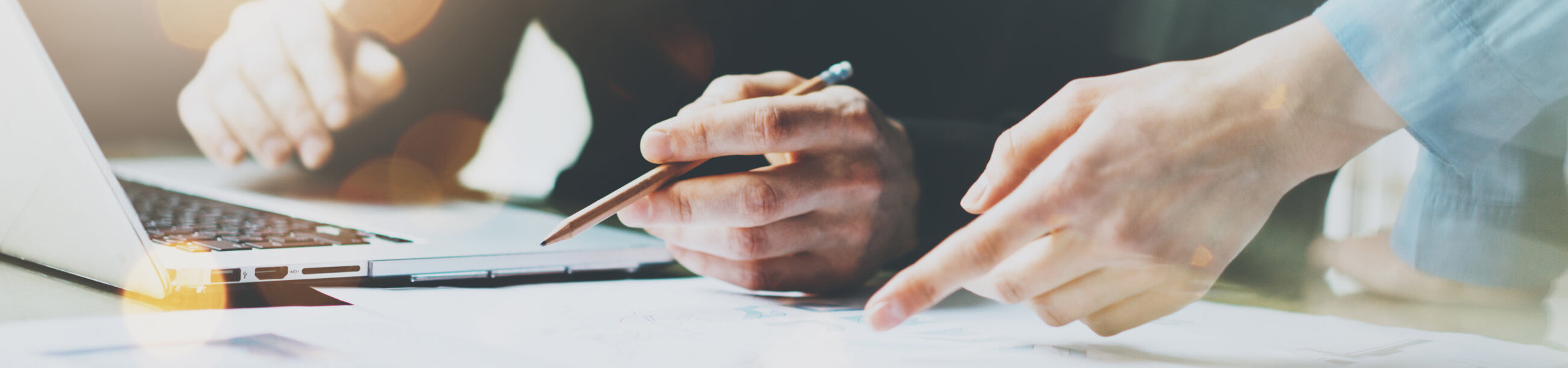 a close up of a hand holding a pencil near a laptop and another hand pointing down